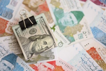 Roll of US dollar bills lies on big amount of Pakistan rupees banknotes close up