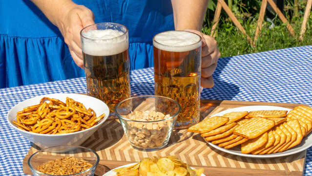 Summertime frothy ale and crispy snacks on a gingham cloth evoke Oktoberfest vibes and National Picnic Day