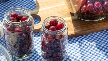 Sunlit jars brimming with plump cherries sparkle on a gingham cloth, evoking midsummer festivities and Cherry Pit Spitting Day