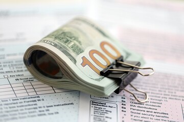 Big amount of United States hundred dollar bills in bunch on table with tax return form