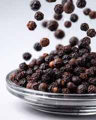 Fototapeta premium Close-up of black peppercorns falling into a glass bowl, showcasing their texture and color