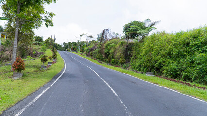 Empty road winding uphill through a tropical landscape with lush green vegetation and a cloudy sky
