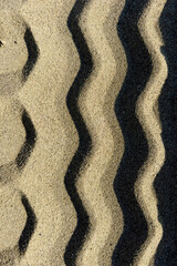 Close-up detail of a geometric pattern of tire tracks on sand