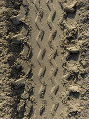 Close-up detail of a geometric pattern of tire tracks on sand