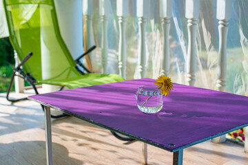 A pleasant summer background with a glass and a flower. The rays of the sun fill a yellow flower in...