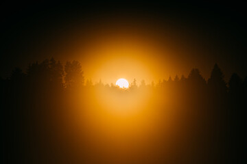 Orange glowing sunset over treeline silhouette across a lake or river with clear sky 