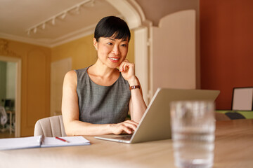 Confident female financial advisor examining reports over laptop while working at desk in corporate...