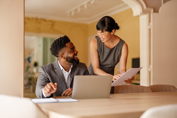 Businesswoman holding financial reports and talking with male colleague at desk in corporate office