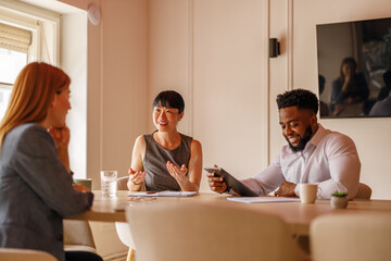 Happy businesswoman with notepad on desk discussing project strategies with colleagues in meeting...