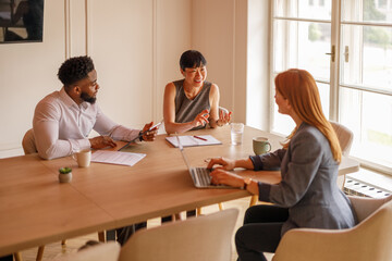 Happy professional colleagues reviewing data and exchanging ideas during team discussion in...