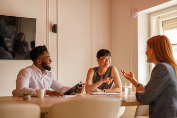 Happy group of coworkers working together on project in board room using computers and documents
