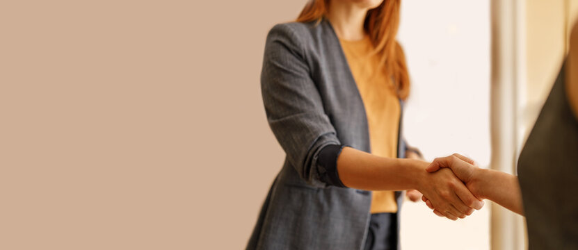 Midsection of female professionals congratulating each other with handshake after successful meeting against wall in office