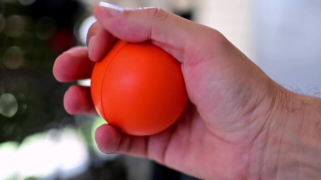Close-up of a man's hand squeezing  an orange anti-stress soft ball into his fist. Selective focus, shallow depth of field.