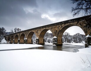 Snowy Landscape with Ancient Stone Bridge Over a Partially Frozen River in Winter