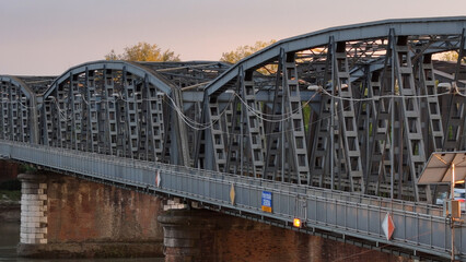 Metal bridge spanning Po River in Cremona, linking riverbanks with arched iron structure and brick...