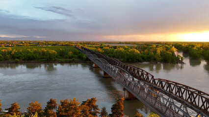 Metal bridge spanning Po River in Cremona, linking riverbanks with arched iron structure and brick...