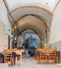 A charming view of a narrow, historic alley in Vieste, Italy, transformed into an inviting outdoor restaurant. Arched stone architecture and warm lighting create a captivating atmosphere, typical of A