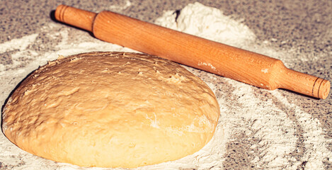 Wooden rolling pin with freshly prepared dough, flour. Rolled dough with rolling pin on table...