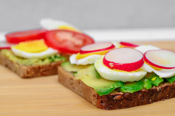 A healthy sandwich made of brown bread with sliced green avocado, hard-boiled egg, radish and tomato