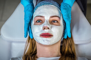 Beauty procedures skin care concept. Doctor applying facial gray mud clay mask on woman face in...