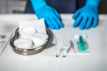 Doctor's hand in blue gloves and ampoule vaccine and syringe on white table. Cosmetology theme