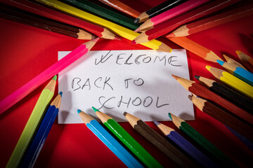 Lápices  de colores sobre un fondo rojo y tarjeta de Bienvenidos de nuevo a la escuela