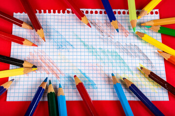 Lápices  de colores sobre una hoja de papel cuadriculada y fondo rojo 