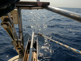 Close-up view of anchor and bow roller system on sailing yacht, with nautical rope and blue sea in...