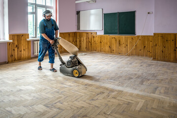 Professional Repairman in blue restoring sanding grinding parquet floor with a sanding machine