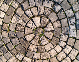 Circular cobblestone pattern with grass growing through ancient stone texture