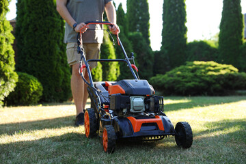 Man cutting green grass with lawn mower in garden, closeup