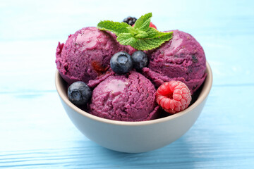 Delicious sorbet with fresh berries and mint in bowl on light blue wooden table, closeup