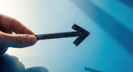 Hand holds black arrow on blue surface, suggesting direction or progress