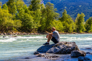 Man smokes a cigarette on rocks by river in Austria.
