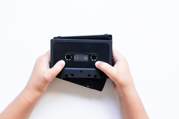 Child hands holding vintage black audio cassettes on white background