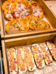 Freshly baked savory flatbreads and stuffed bread rolls displayed in a wooden crate at a bakery during morning hours