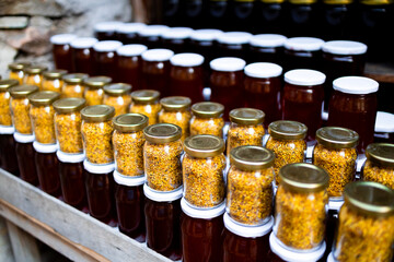 Assorted honey and pollen jars displayed on wooden shelf in rustic setting