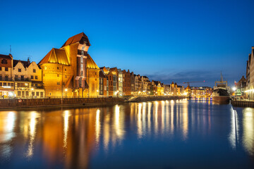 Gdansk with medieval port crane over The Motlawa river, a city on the Baltic coast of northern Poland, Europe. Night Cityscape: Reflections of old buildings on a river under the dark blue sky.