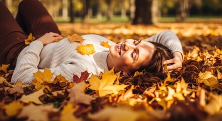 Smiling woman lies in fallen autumn leaves, sunlight