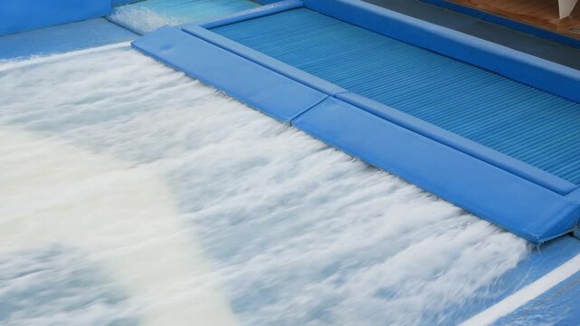 water flowing of artificial flowboarding waves. The water flows up and over surfaces engineered to replicate the shape of ocean waves under sunny daytime without any people