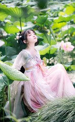 Serene young woman in traditional dress among lotus flowers.