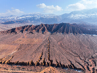 An aerial drone shot of the dramatic red Mars Canyon landscape with deep eroded ravines and snow...