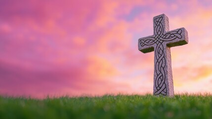 Stone Cross on Green Grass Against a Colorful Sunset Sky with Pink and Purple Hues