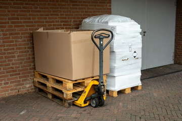 Pallet jack lifting cardboard box on wooden pallets near warehouse loading dock