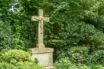 Stone crucifix standing in green bushes in cemetery or garden