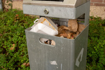 Public trash can overflowing with garbage and food containers in a park