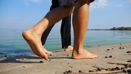 Bare feet of couple stepping together along sand beach at coastline. Male and female legs of pair walking near seaside. Happy lovers going along sandy shore. Concept of summer vacation or holiday