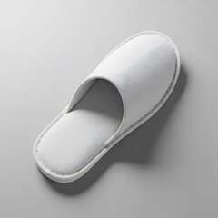 A clean single white terry cloth hotel slipper isolated on a neutral gray background from a top view