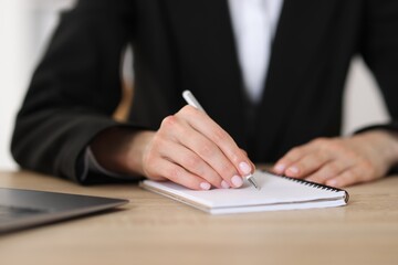 Woman writing in notepad with pen at wooden table, closeup