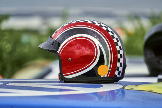 Classic racing helmet with red, black and checkered design sits on top of a blue car, evoking speed, competition, and safety on the racetrack - Powered by Adobe